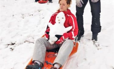 Femme en blouson rouge sur une luge dans la neige avec bonhomme de neige